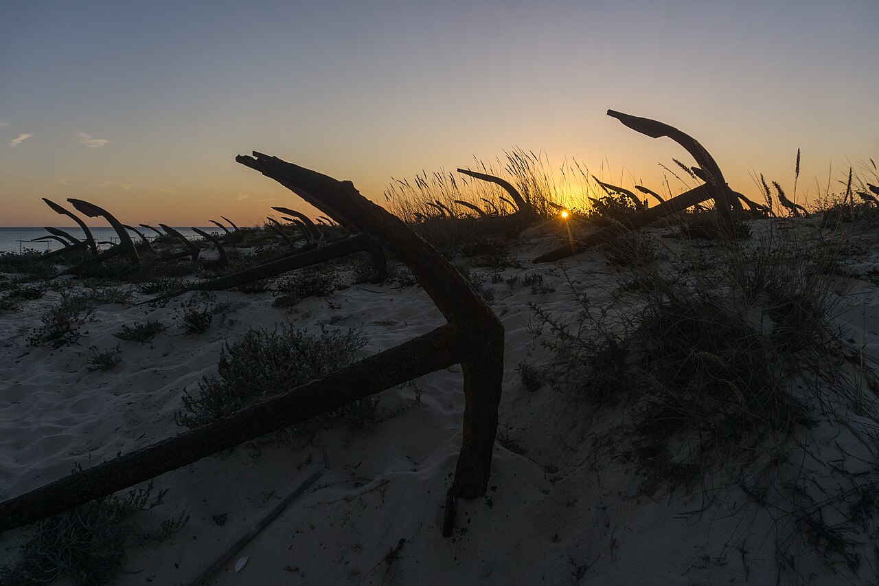 Rows of old tuna-fishing anchors in the dunes at Praia do Barril, Tavira, at sunset